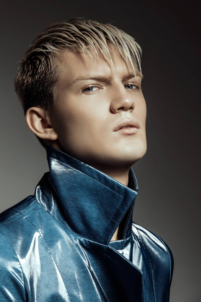 Knappe gestripte blonde mannelijk model dragen blauwe vacht op grijs geïsoleerd lettertype achtergrond - Foto, afbeelding
