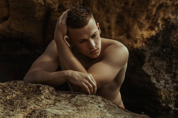 Strong face male model on the nature background with rocks and water on the beach on the sunset - Fotó, kép
