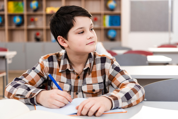 Étudiante brune pensive en chemise à carreaux écrivant dans un carnet de notes pendant les cours
 - Photo, image