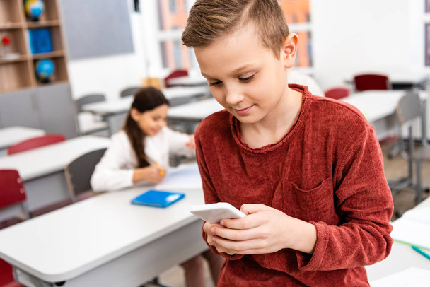 Kiinnostunut koulupoika seisoo luokassa ja käyttää älypuhelinta jarrutuksen aikana
  - Valokuva, kuva