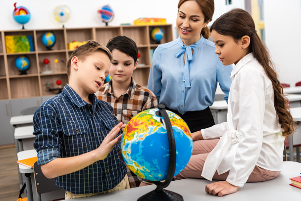Leraar en leerlingen raken Globe met glimlach tijdens het studeren Geografie in de klas - Foto, afbeelding