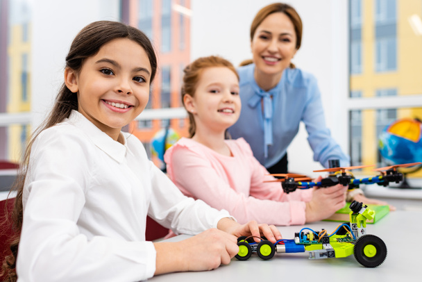 Smiling teacher standing near pupils with educational toys in classroom - Photo, Image