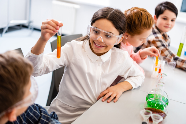Alumnos con gafas protectoras sosteniendo frascos durante la lección de química
 - Foto, Imagen