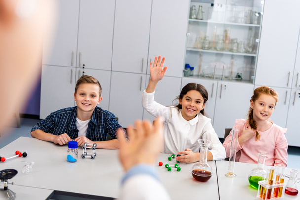 Hymyilevä koulutyttö nostaa kätensä luokassa kemian tunnin aikana
 - Valokuva, kuva