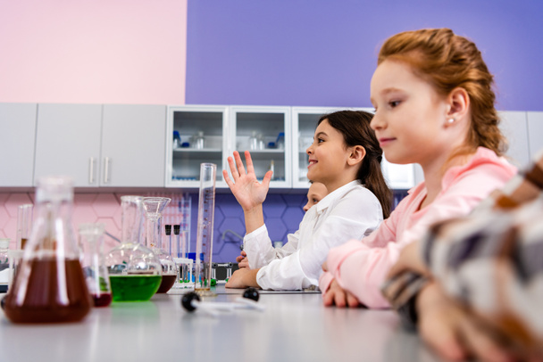 Colegiala sonriente levantando la mano en clase durante la lección de química
 - Foto, Imagen