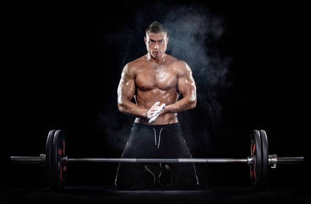 Foto de fuerte musculoso culturista atlético hombre bombeando los músculos con barra sobre fondo negro. Concepto de culturismo de energía de entrenamiento
. - Foto, imagen