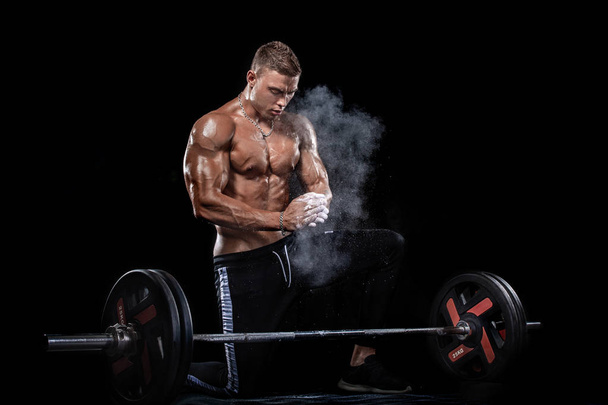 Photo of strong muscular bodybuilder athletic man pumping up muscles with barbell on black background. Workout energy bodybuilding concept. - Photo, Image