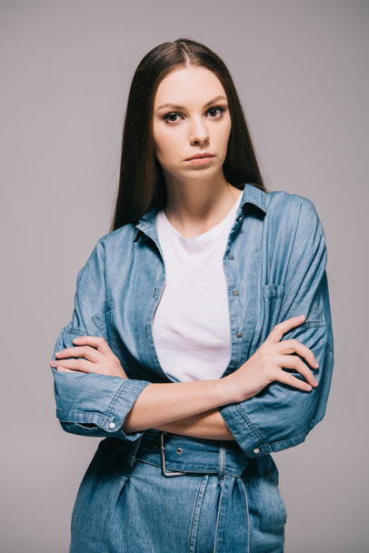 young adult and beautiful woman in denim dress with crossed arms isolated on grey - Photo, Image