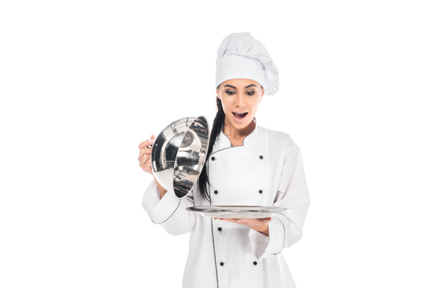 Shocked chef in hat holding tray with cloche isolated on white - Фото, зображення