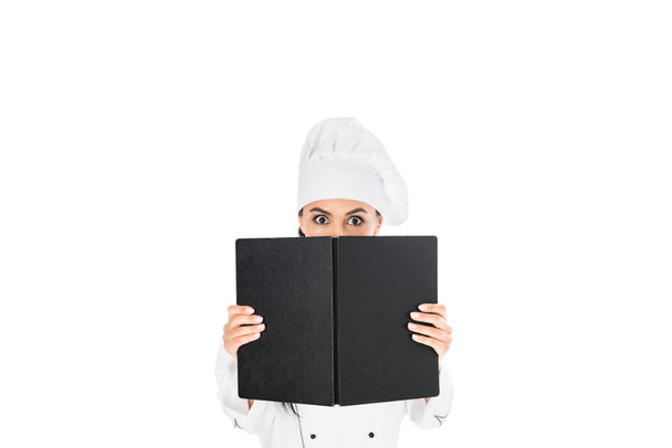 Shocked chef in uniform holding black book isolated on white - Zdjęcie, obraz