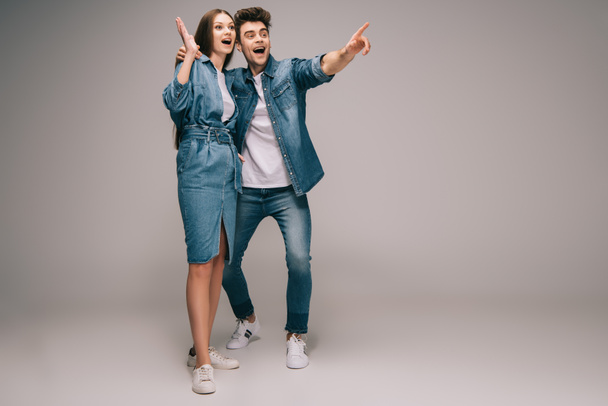 surprised girlfriend in denim dress and smiling boyfriend in jeans and shirt pointing with finger  - Фото, изображение