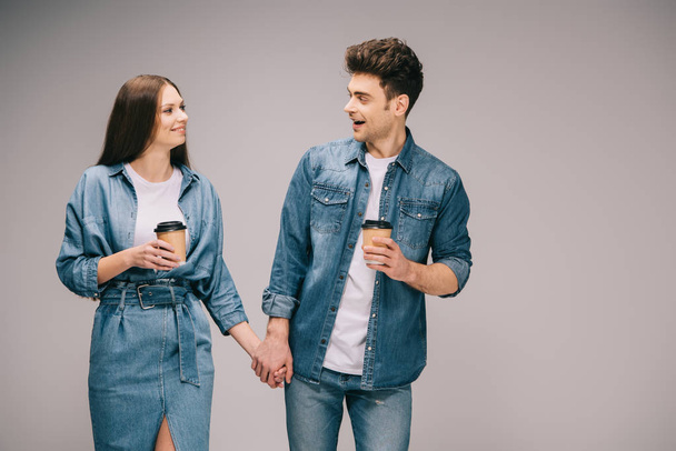 girlfriend in denim dress and handsome boyfriend in jeans and shirt holding paper cups looking at each other  - Фото, изображение