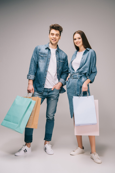 girlfriend in denim dress and handsome boyfriend in jeans and shirt holding shopping bags and looking at camera  - 写真・画像