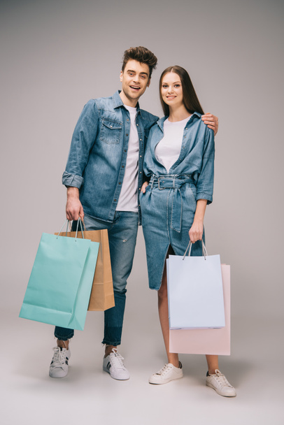 girlfriend in denim dress and handsome boyfriend in jeans and shirt holding shopping bags and looking at camera  - Фото, зображення