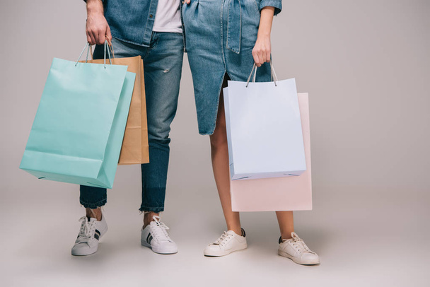 cropped view of man and woman holding shopping bags on grey background  - Foto, Bild