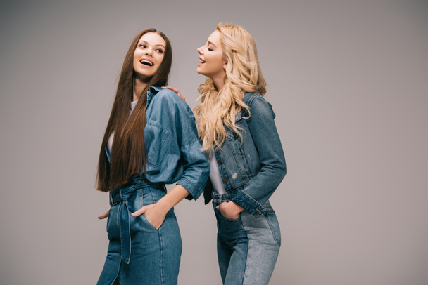 blonde and brunette women in denim clothes smiling on grey background  - 写真・画像