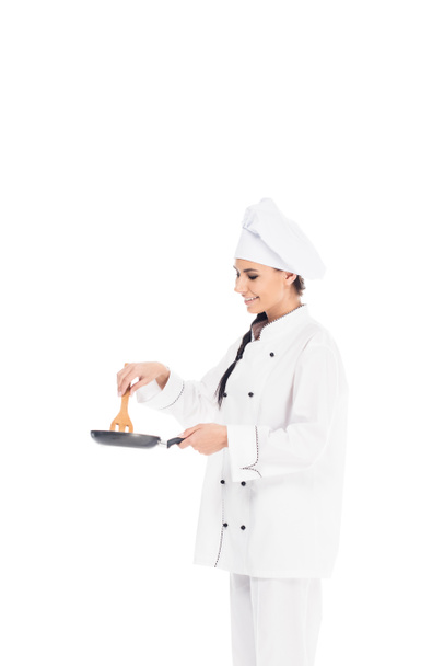 Шеф-повар в шляпе держит сковородку и деревянную кухонную лопатку, изолированную на белом
 - Фото, изображение