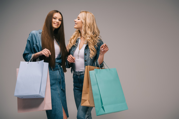 happy blonde and brunette women in denim clothes smiling and holding shopping bags  - Photo, Image