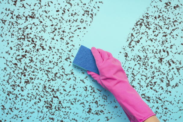 Женская рука в розовых перчатках держит губку для стирки и удаляет грязь с поверхности на синем фоне. Концепция клининговых услуг. Плоский, вид сверху
 - Фото, изображение