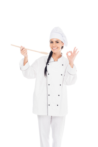 Chef sonriente en uniforme sosteniendo espátula de madera y mostrando el cartel de bien aislado en blanco
 - Foto, imagen
