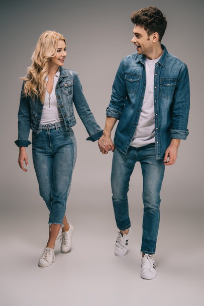 happy boyfriend and smiling girlfriend in denim clothes holding hands and looking at each other  - Fotó, kép