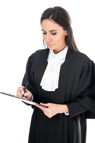 Geconcentreerde rechter in justitiële gewaad schrijven in klembord geïsoleerd op wit - Foto, afbeelding