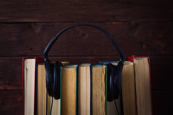 Auriculares colocados en libros plegados sobre el fondo de madera oscura
 - Foto, imagen