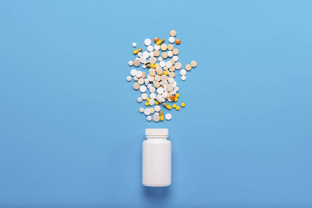 Valkoinen pullo ja monivärinen pillereitä sinisellä taustalla. Käsitys lääkkeistä, lääkkeistä, lääkkeistä ja sairauksien hoidosta. Tasainen, ylhäältä
 - Valokuva, kuva