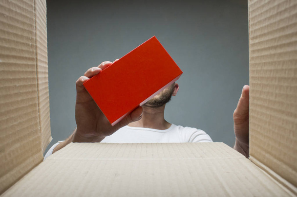 Ein Mann nimmt eine kleine Schachtel mit einer Bestellung aus einer offenen Lieferbox. Innenansicht. Konzept erhielt ein Paket, Bestellung, Internet-Mogazin, Lieferung von Waren, Online-Shopping. - Foto, Bild