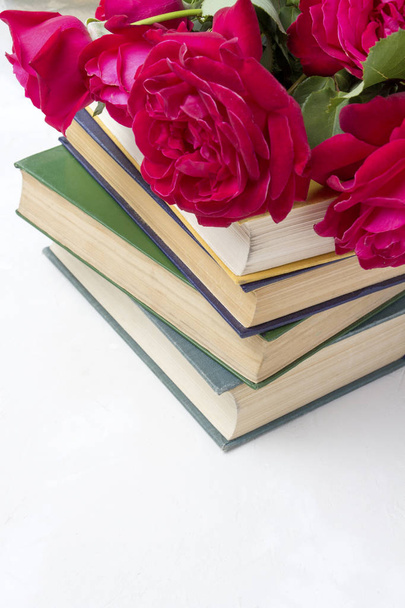 A bouquet of red roses on a pile of books on a light stone background. Concept love of literature and romance novels - Photo, Image