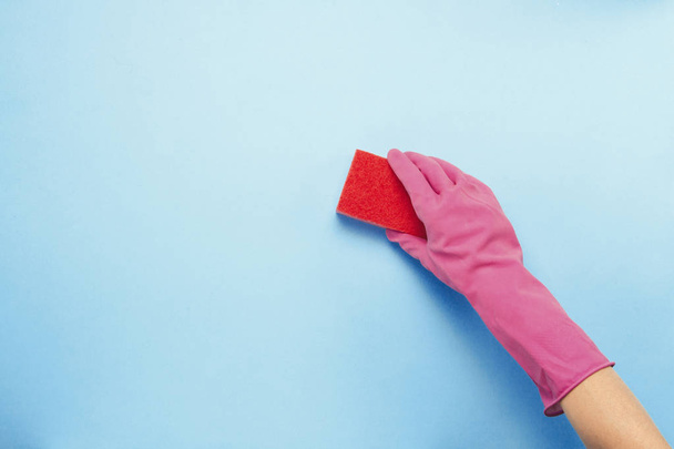 Mano femenina en guantes rosados con esponja para limpiar sobre fondo azul. concepto de servicio de limpieza. Piso tendido, Vista superior
 - Foto, imagen