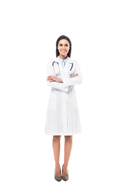 Full length view of joyful doctor in white coat standing with folded arms isolated on white - Foto, immagini