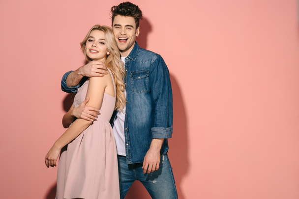 smiling girlfriend and handsome boyfriend in denim shirt hugging and looking at camera  - Photo, Image