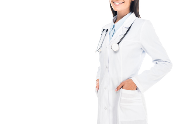 Vista ritagliata del medico sorridente con stetoscopio in piedi con le mani in tasche isolate su bianco
 - Foto, immagini