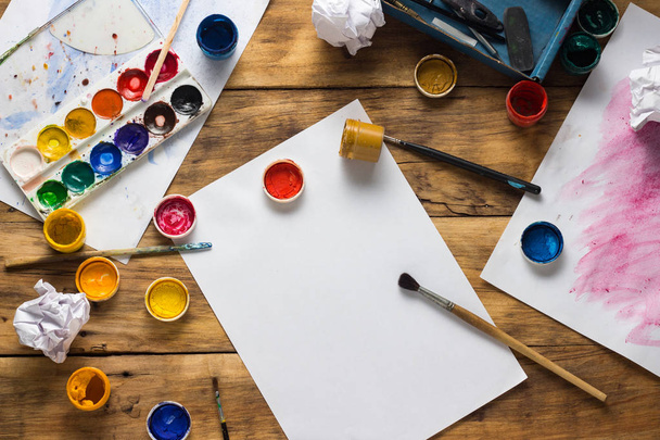 Ressamın işyeri, ahşap bir arka planda suluboya boya, guaj, fırça ve kağıt yapraklarıyla. Uzayı kopyala Düz yatış, üst görünüm - Fotoğraf, Görsel