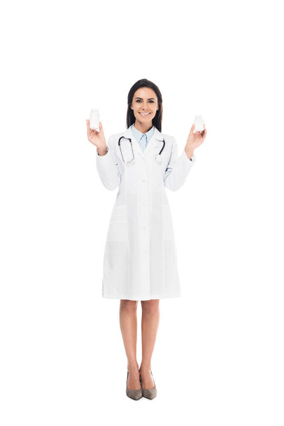 Full length view of doctor in white coat with stethoscope holding pills isolated on white - 写真・画像