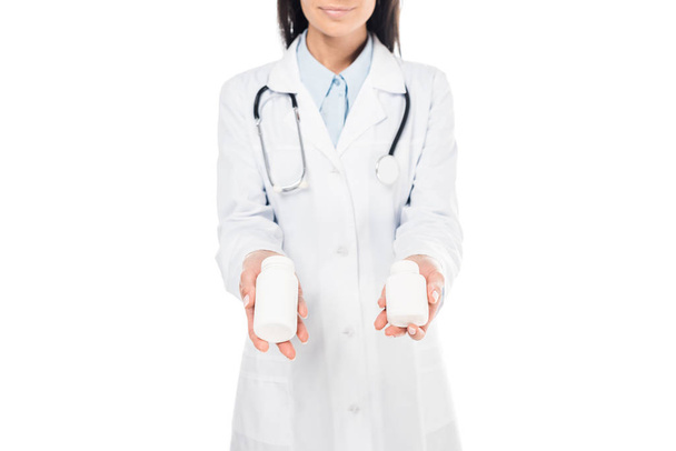 Vue recadrée du médecin en manteau blanc avec stéthoscope tenant des pilules isolées sur blanc
 - Photo, image