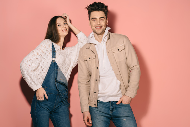 brunette and beautiful girlfriend in denim overalls and handsome boyfriend smiling and looking at camera  - Fotografie, Obrázek