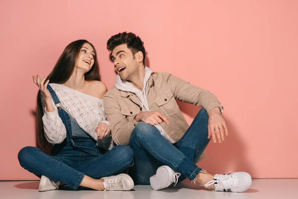 brunette and beautiful girlfriend in denim overalls and handsome boyfriend sitting on floor and looking at each other  - Фото, зображення