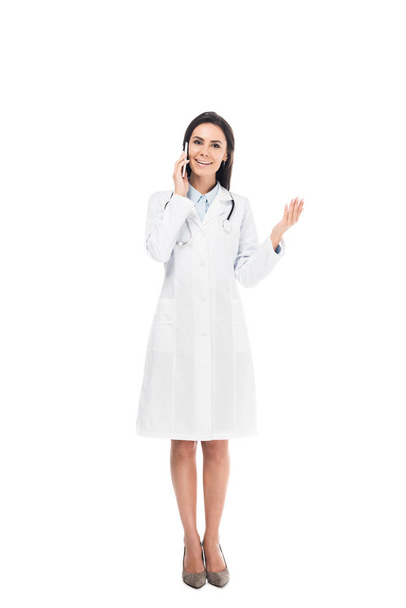 Full length view of doctor in white coat with stethoscope talking on smartphone isolated on white - Fotó, kép