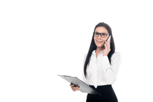Businesswoman in glasses talking on smartphone and holding clipboard isolated on white - Foto, afbeelding