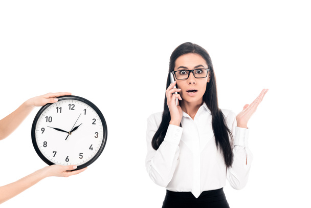 Shocked businesswoman talking on smartphone near clock isolated on white - Fotografie, Obrázek