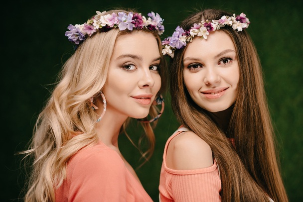 attractive brunette and blonde women in wreaths smiling and looking at camera  - Фото, зображення