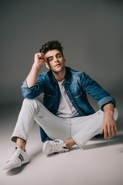 handsome man in denim shirt and jeans sitting on floor and looking at camera  - Foto, afbeelding