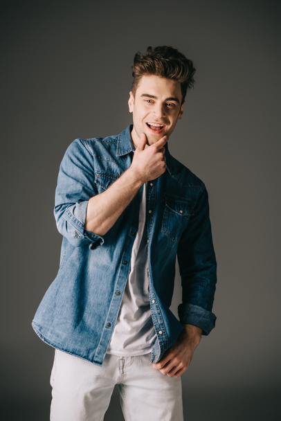 smiling and handsome man in denim shirt and jeans looking at camera on grey background  - Fotó, kép