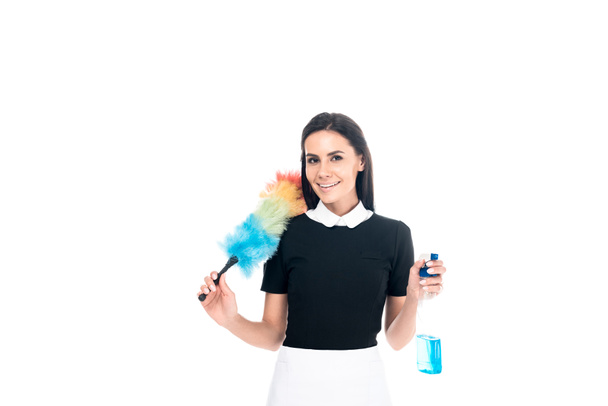 Brunette maid in uniform holding duster and spray bottle isolated on white - Photo, Image