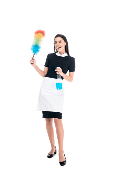 Full length view of brunette housemaid in uniform holding duster and spray bottle isolated on white - Foto, afbeelding