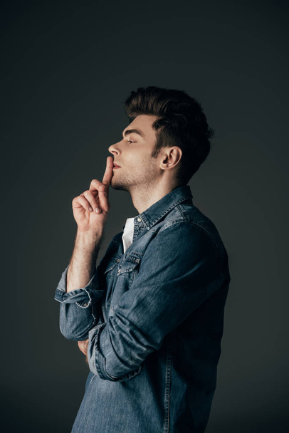side view of handsome and brunette man in denim shirt showing shh gesture isolated on black - Foto, Bild