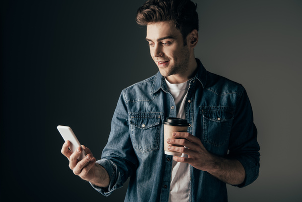 handsome man in denim shirt holding paper cup and using smartphone  - Фото, зображення
