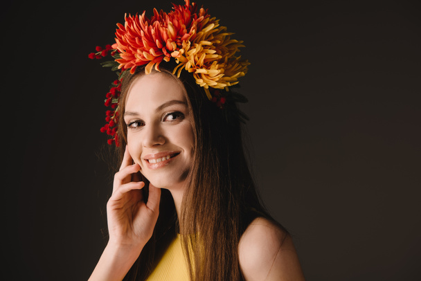 beautiful and smiling woman in wreath looking at camera isolated on black  - Фото, изображение